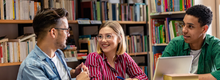 Three students smiling studying in library